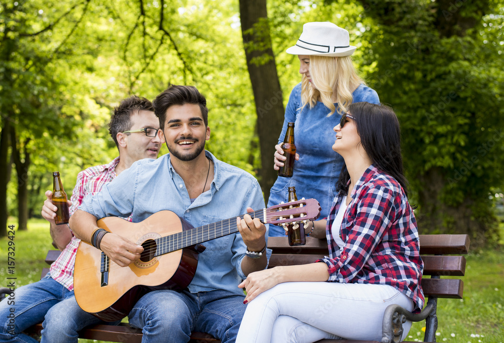 Group of friends having fun in the park while playing guitar.