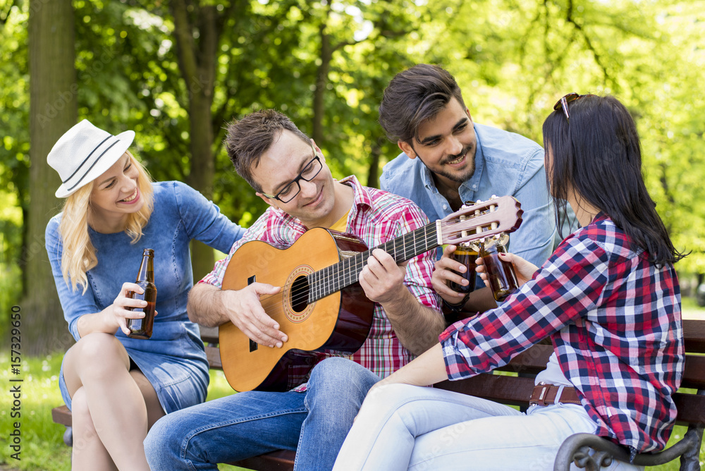 Group of young people having fun in the park while playing guitar and drinking beer