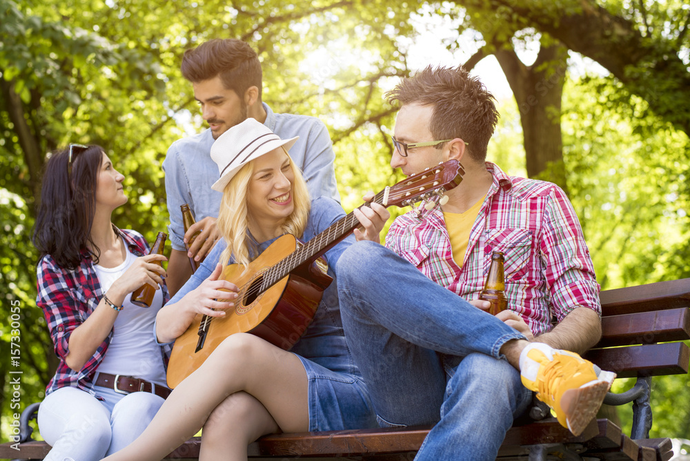 Group of friends having fun in the park while playing guitar.