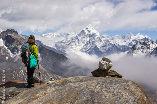 Young Woman hiker with backpack and hiking poles is standing and looking on Ama Dablam mountain. Cloudy sky. Himalaya, Nepal. photo