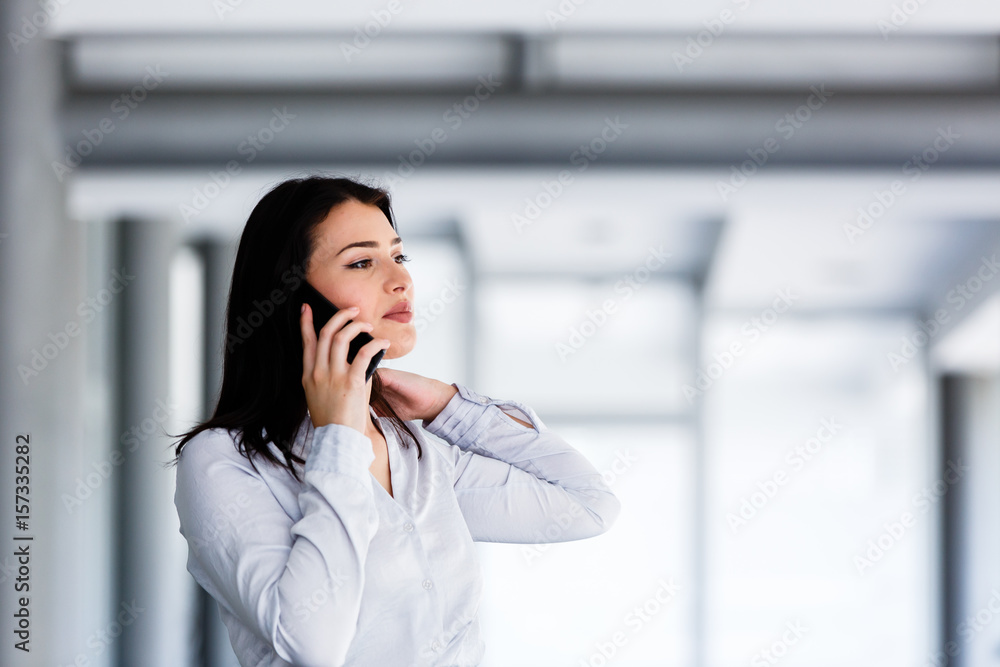 Attractive woman standing while talking on phone in business building Attractive woman standing while talking on phone in business building