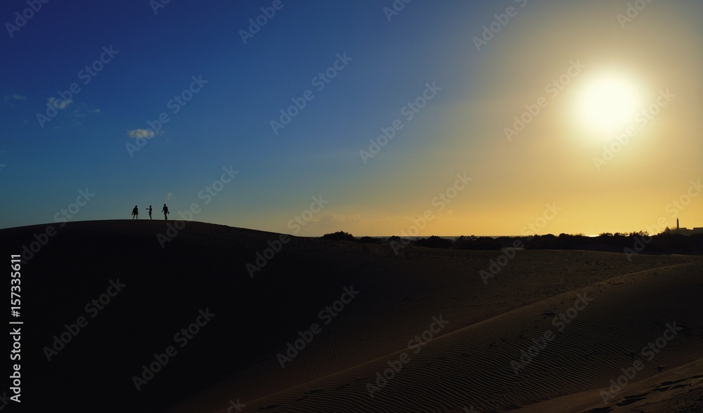 Obraz premium People on the sandy mountain. Sunset in the background.