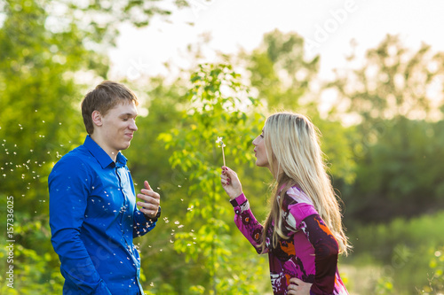 Couple in love blowing blowballs flowers in faces of each other. Smiling and laughing people having good time outside on summer warm day. Woman and man enjoying nature.