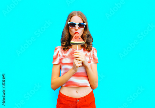 Fashion pretty woman is eating a slice of watermelon in the form of ice cream a colorful blue background