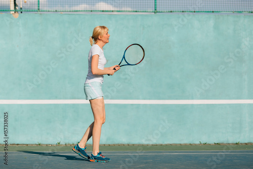 Tennis player playing on the court on a sunny day. Young sport woman training outdoors. Healthy lifestyle concept. © beatleoff