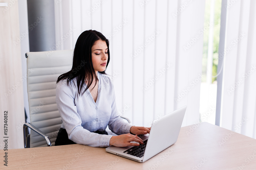 Attractive woman sitting in office and typing on her laptop Attractive woman sitting in office and typing on her laptop