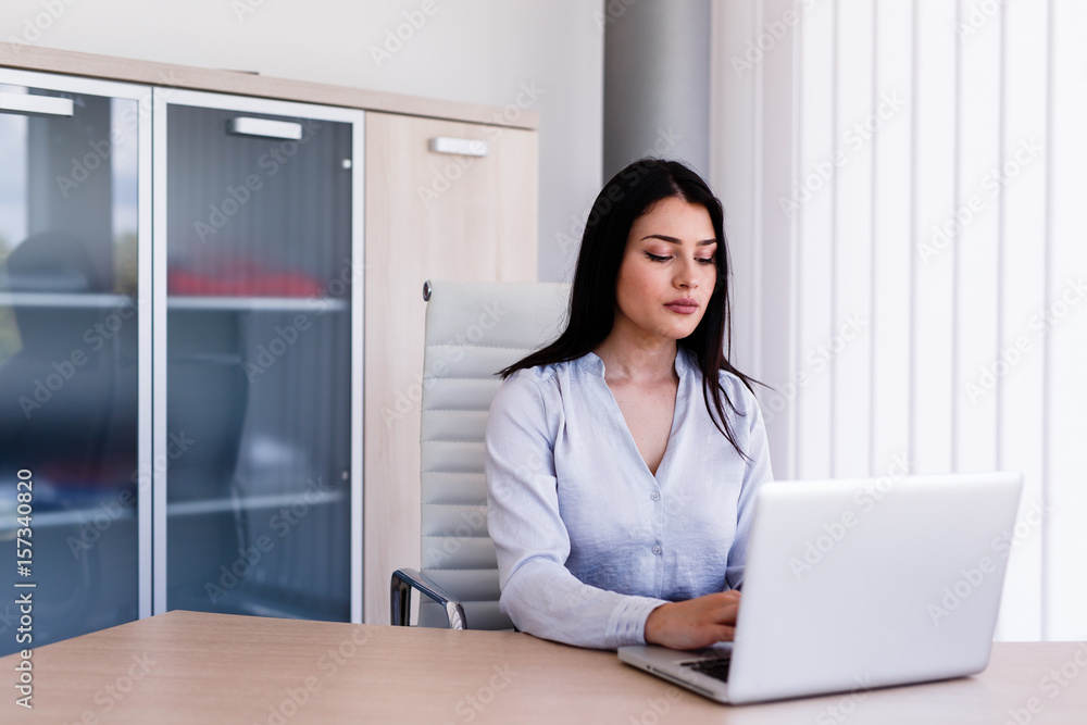 Attractive woman sitting in office and typing on her laptop Attractive woman sitting in office and typing on her laptop
