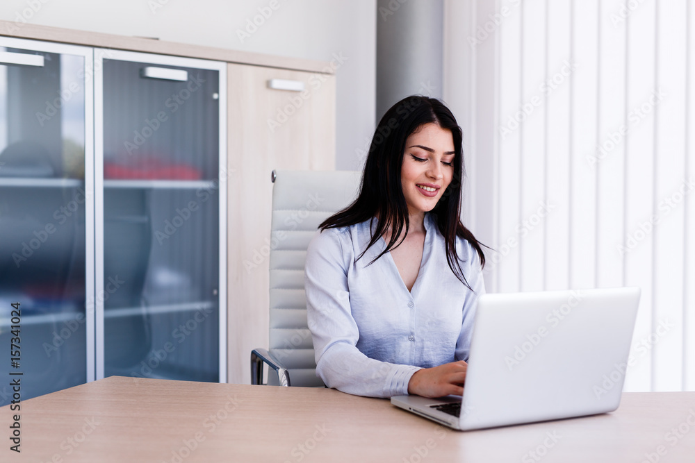 Attractive woman sitting in office and typing on her laptop Attractive woman sitting in office and typing on her laptop