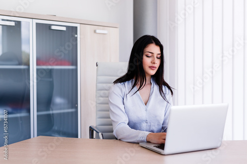 Attractive woman sitting in office and typing on her laptop