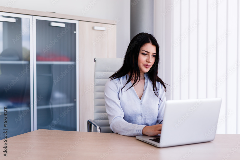 Attractive woman sitting in office and typing on her laptop Attractive woman sitting in office and typing on her laptop