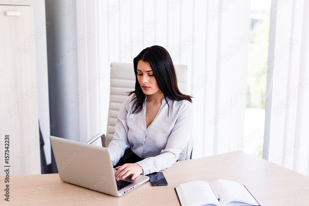 Attractive woman sitting in office and typing on her laptop Attractive woman sitting in office and typing on her laptop
