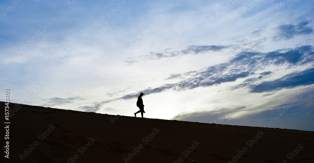 Silhouette man walking down desert  with clouds blue sky background in the morning