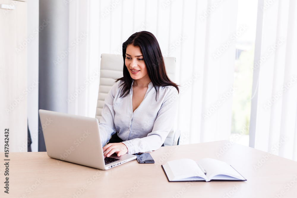 Attractive woman sitting in office and typing on her laptop Attractive woman sitting in office and typing on her laptop