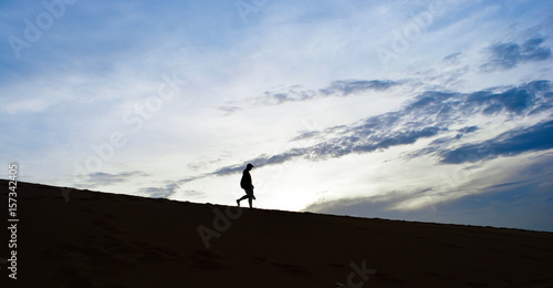 Silhouette man walking down desert with clouds blue sky background in the morning
