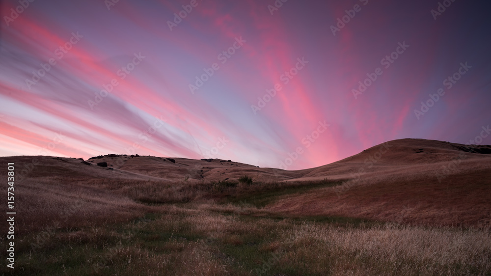 Colorful sunset with grassy hills and rocks