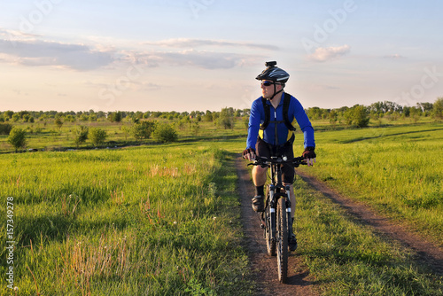 cyclist rides on the road in a field on a bright sunny day.