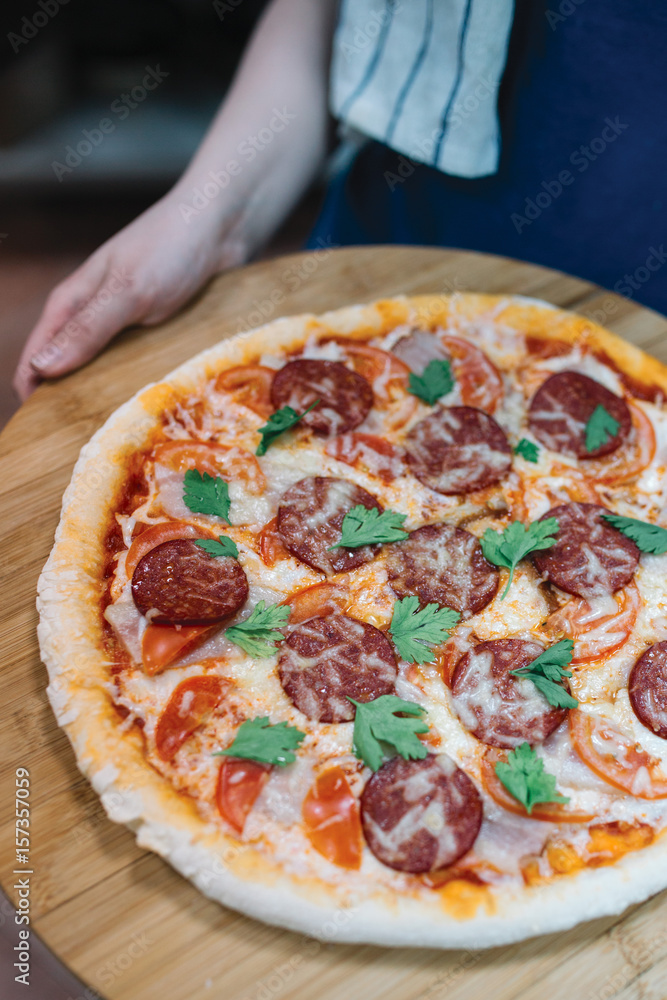 Pizza with salami, cheese, tomatoes and herbs on wooden plate
