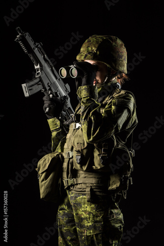 Portrait of armed woman with camouflage. Young female soldier observe with binoculars. Child soldier with gun in war, black background. Military, army people concept