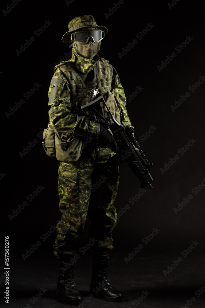 Portrait of armed woman with camouflage. Young female airsoft sniper observe with firearm. Soldier with gun in war, black background.  Military, army people concept