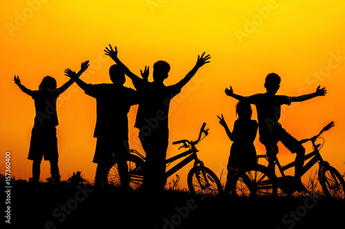 Boys and girls standing and sitting behind a bike with sunset Silhouette. © Akira Kaelyn