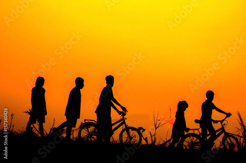 Boys and girls standing a bike with sunset Silhouette.