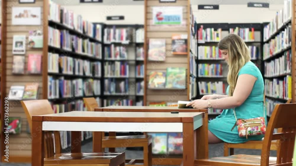 Wide shot of attractive blonde in library reading generic book Wide shot of attractive blonde in library reading generic book