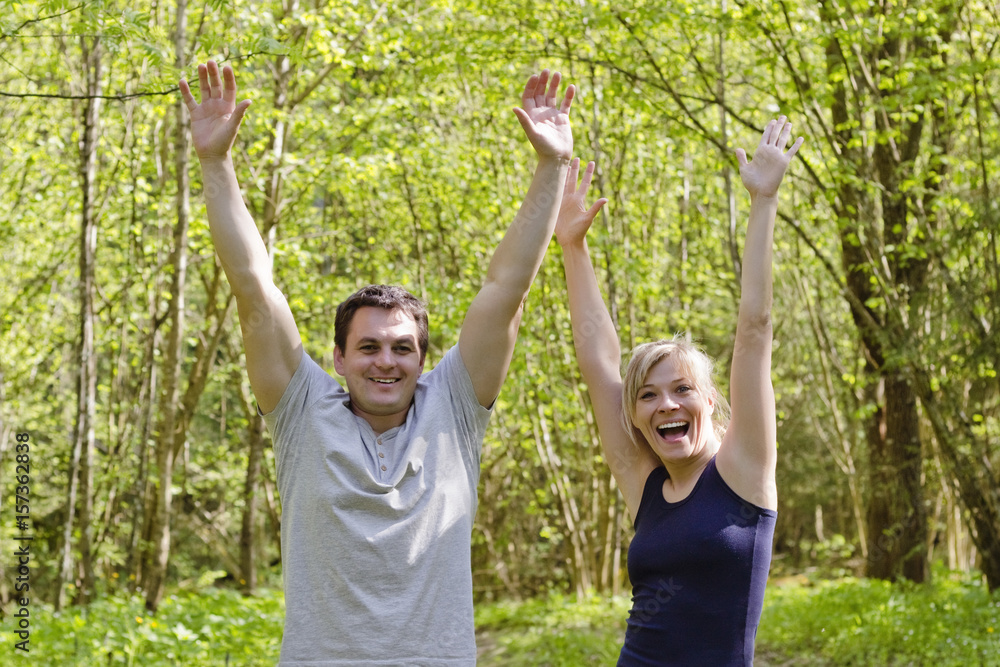Happy joyful couple is happy in the park in hand raises his hands up,victory,win,bright colored Happy joyful couple is happy in the park in hand raises his hands up,victory,win,bright colored