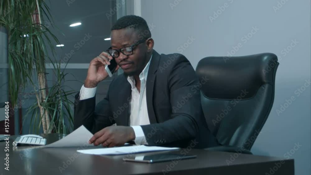 Afro-american businessman examining charts and talking on the phone Afro-american businessman examining charts and talking on the phone