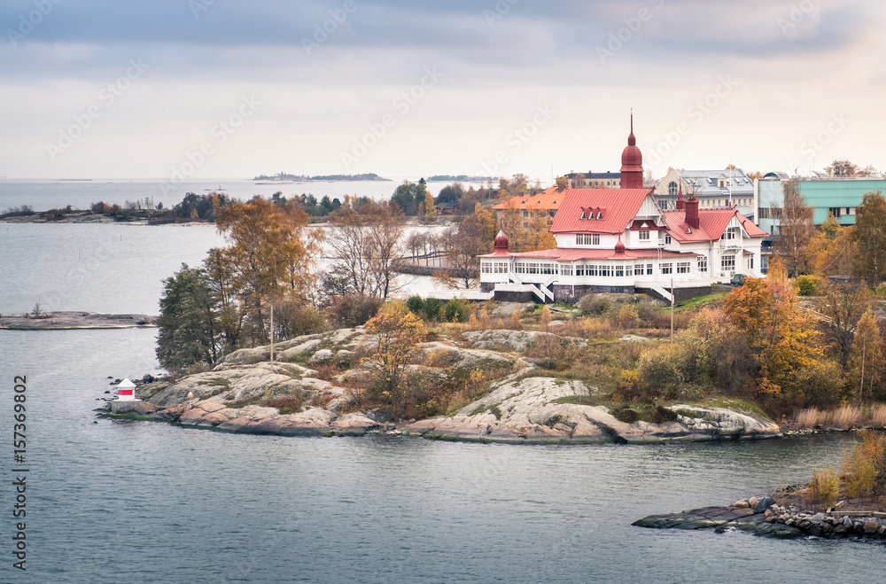 Obraz premium HELSINKI, FINLANDIA - 13 października 2016: Widok z idyllicznej wyspy z ładnym budynkiem na wybrzeżu Helsinek. Pochmurny dzień.