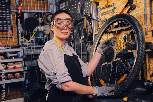 Fototapeta Naklejka Na Ścianę i Meble -  Portrait of female bicycle mechanic over tool stand background.