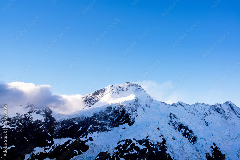 clouds above a snowy steep peak of the mountains of the aoraki mount cook national park in the south island of New Zealand during a sunny day