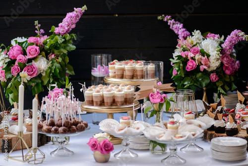 The wedding composition of delicious sponge fruit cakes decorated with juicy cherries and strawberries and are placed on the wooden table.
