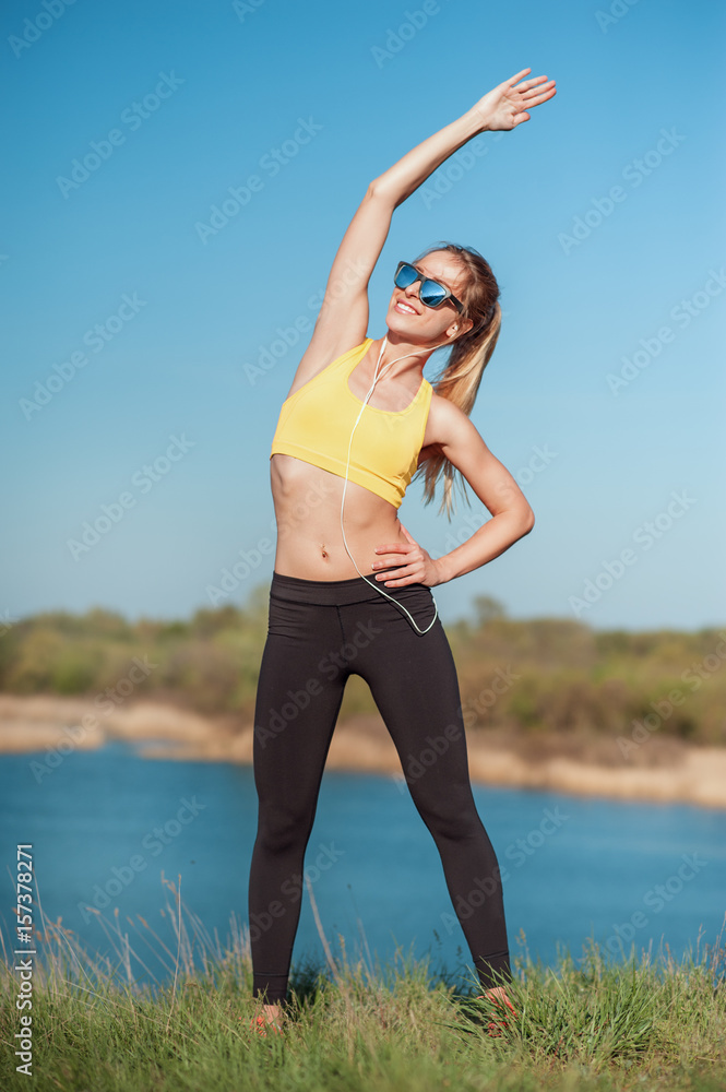 Healthy lifestyle and sport concepts. Woman in fashionable sportswear and sunglasses is doing exercise on nature. Girl on sunny day background. Stretching after training in grass. Great day for sport. Healthy lifestyle and sport concepts. Woman in fashionable sportswear and sunglasses is doing exercise on nature. Girl on sunny day background. Stretching after training in grass. Great day for sport.