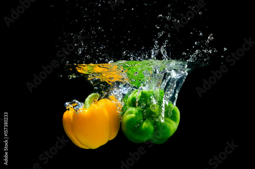 Yellow and green peppers splashing water on black background