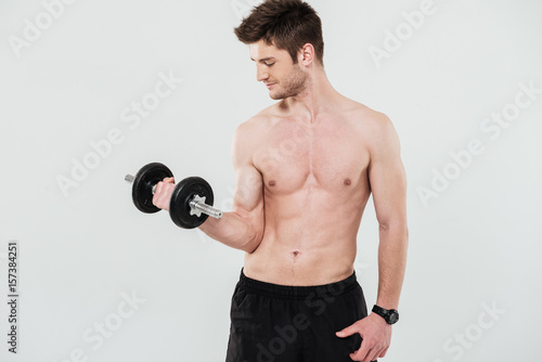Young shirtless sportsman doing exercises with a dumbbell