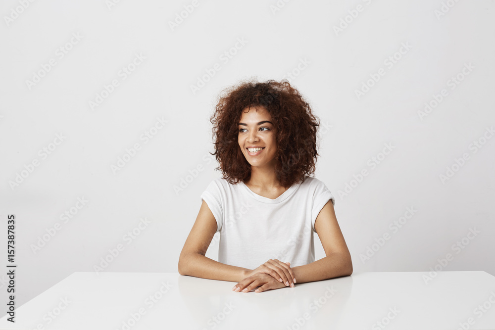 Beautiful african girl smiling laughing sitting over white background. Copy space. Beautiful african girl smiling laughing sitting over white background. Copy space.