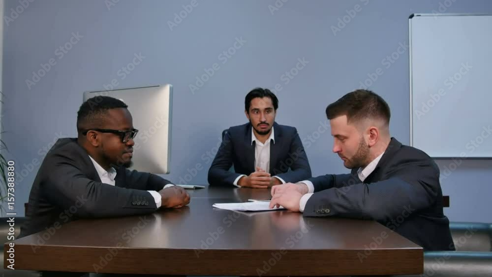 Young serious man holding papers, reading them attentively, during meeting in office Young serious man holding papers, reading them attentively, during meeting in office