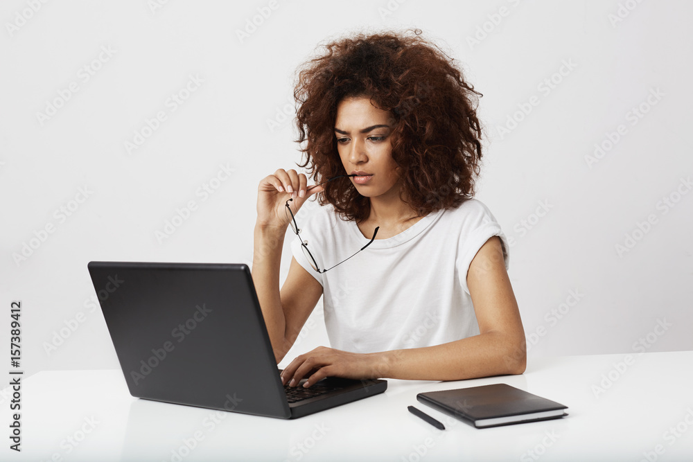 African businesswoman looking at laptop screen thinking over white background. African businesswoman looking at laptop screen thinking over white background.