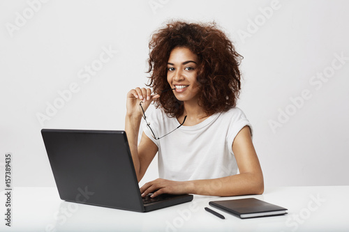 African girl smiling looking at camera sitting at wokplace with laptop. photo