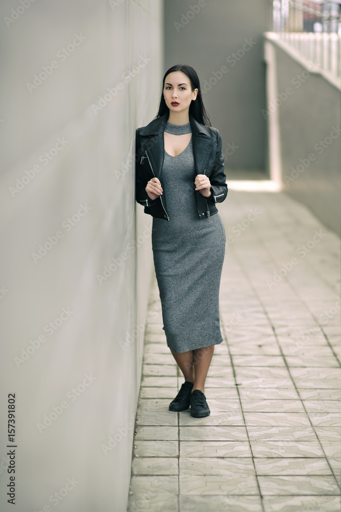 portrait of fashionable girl in long gray dress. Face brunette in black leather jackets with ruby lips on a background of stone portrait of fashionable girl in long gray dress. Face brunette in black leather jackets with ruby lips on a background of stone