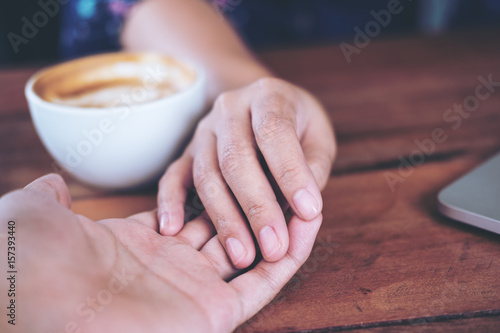 A man and a woman holding each other hands with feeling love on wooden table background