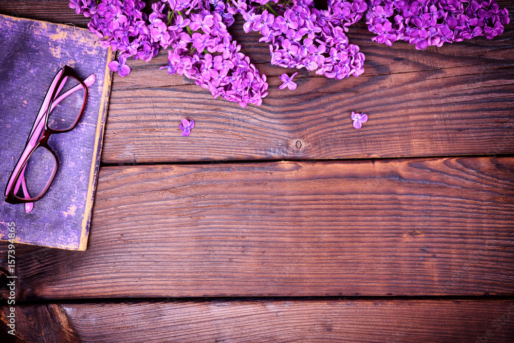branch of a purple lilac and an old book with glasses