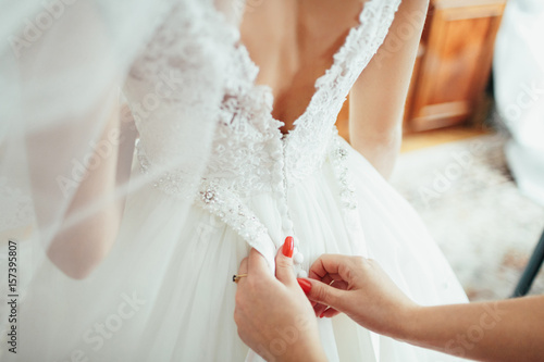 Woman with red nails fixes dress on bride's back