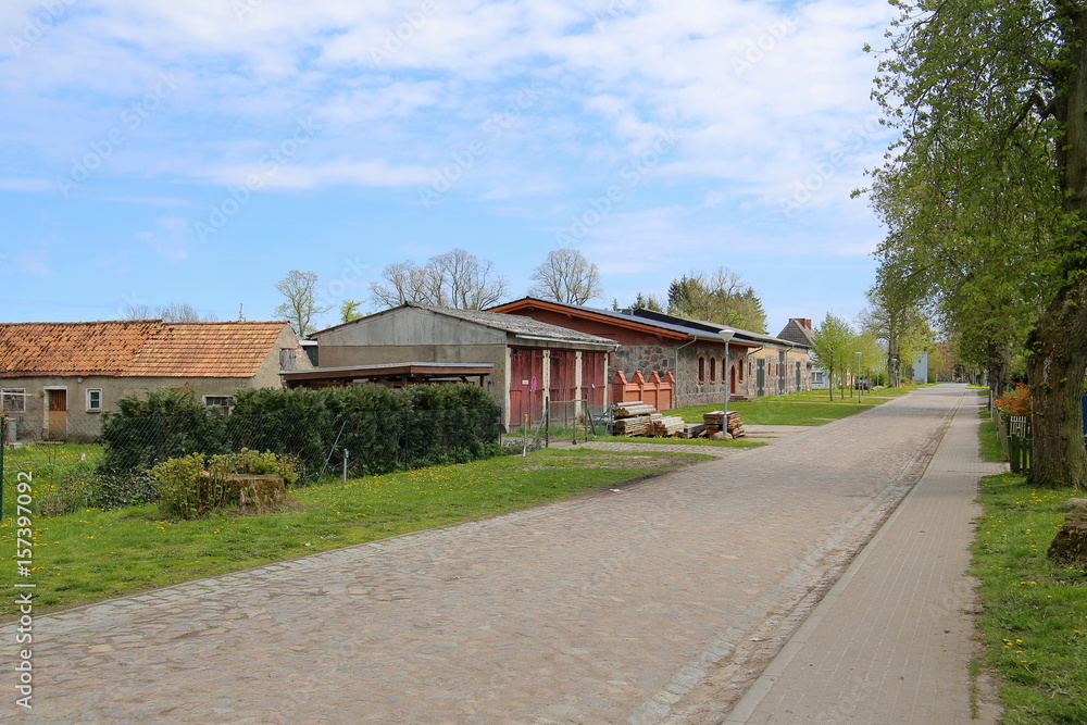 Cobblestone street with buildings belonging to the manor grounds in Behrenhoff, listed as monument