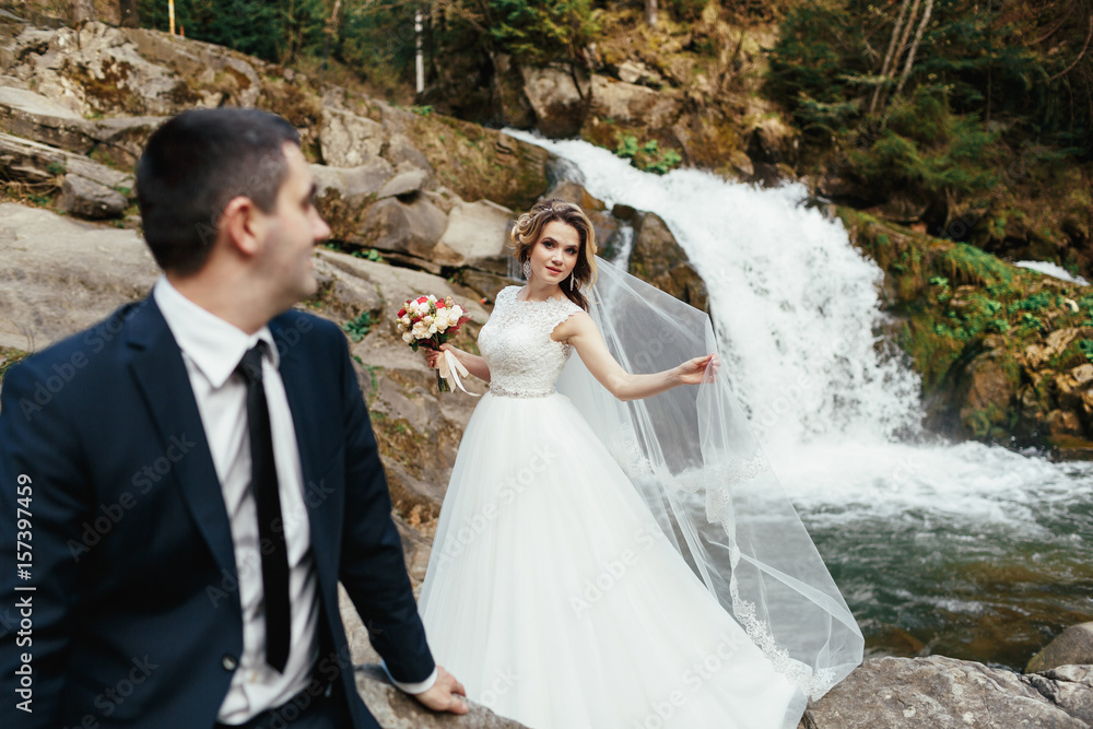 Bride in a magnificent dress stands behind her groom on the stones Bride in a magnificent dress stands behind her groom on the stones