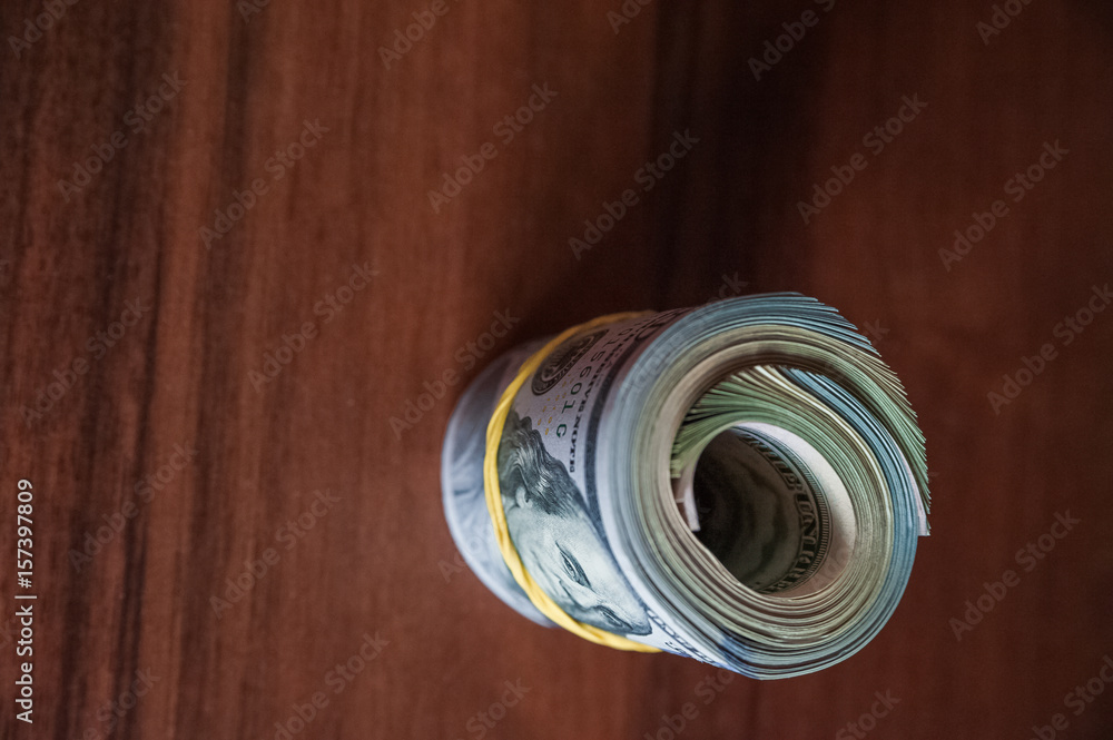 A lot of money on a wooden background. US dollars on one banknote, scattered, with a rubber band A lot of money on a wooden background. US dollars on one banknote, scattered, with a rubber band