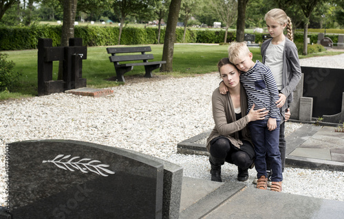 Fotografie Young widow visiting graveyard with kids