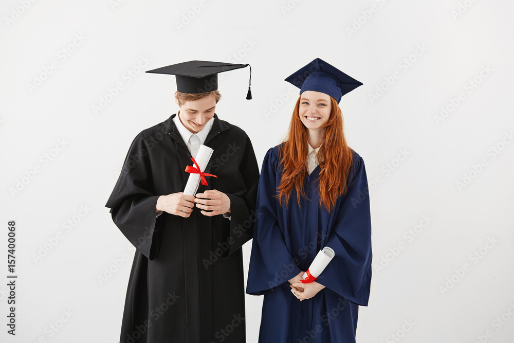 Happy graduates of college in mantles smiling holding diplomas over white background. Happy graduates of college in mantles smiling holding diplomas over white background.
