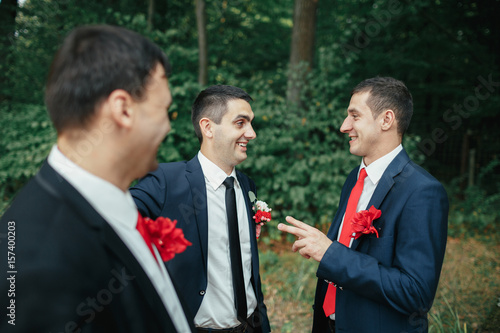 Cheerful groom and groomsmen talk in the forest