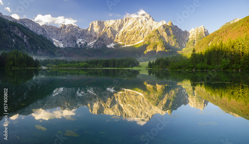Panoramic view of beautiful white winter wonderland scenery in the Alps with mountain summits reflecting in crystal clear mountain lake on a colorful dawn